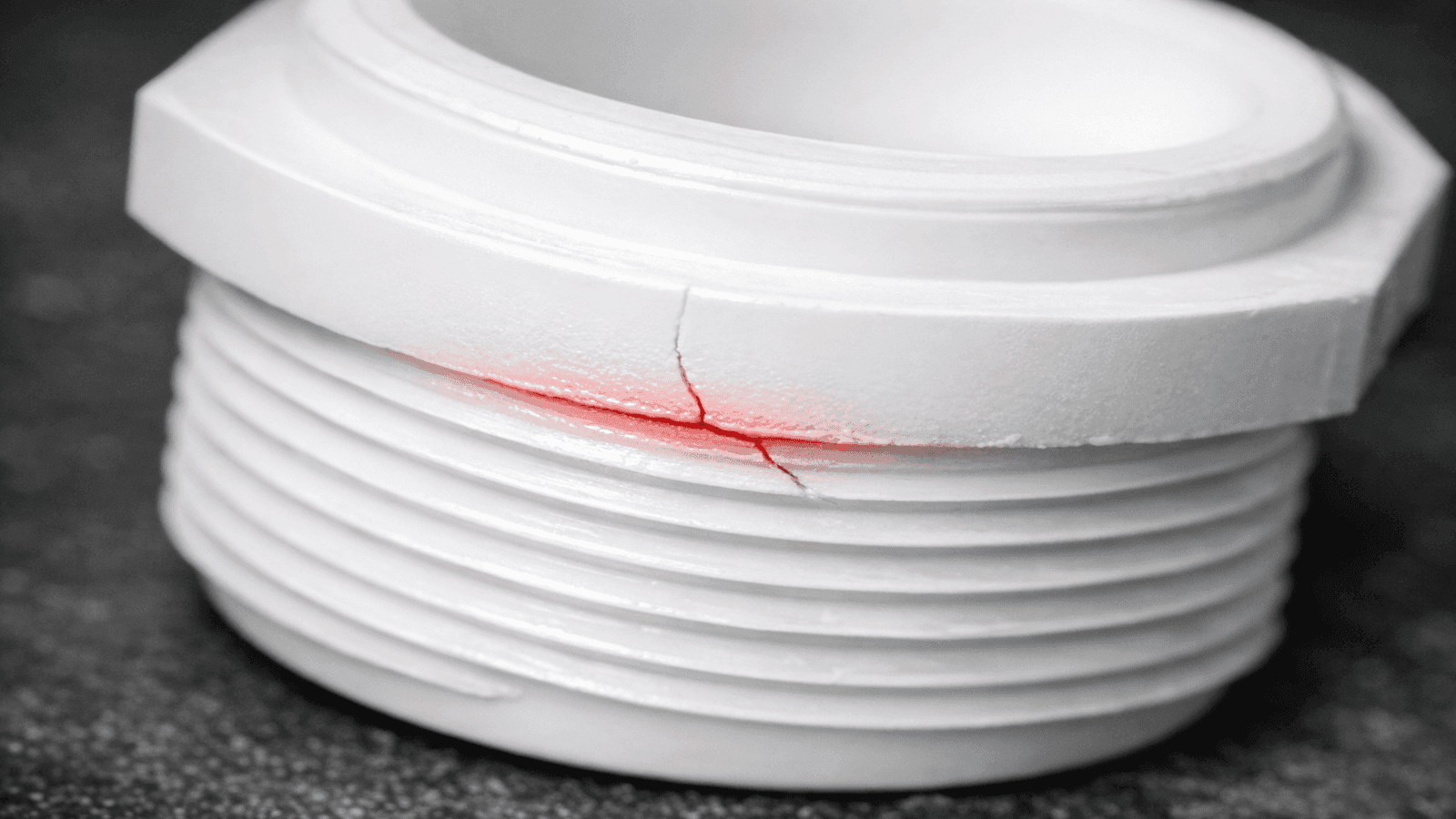 Close-up of a cracked white PVC pipe fitting caused by overtightening during a DIY plumbing repair