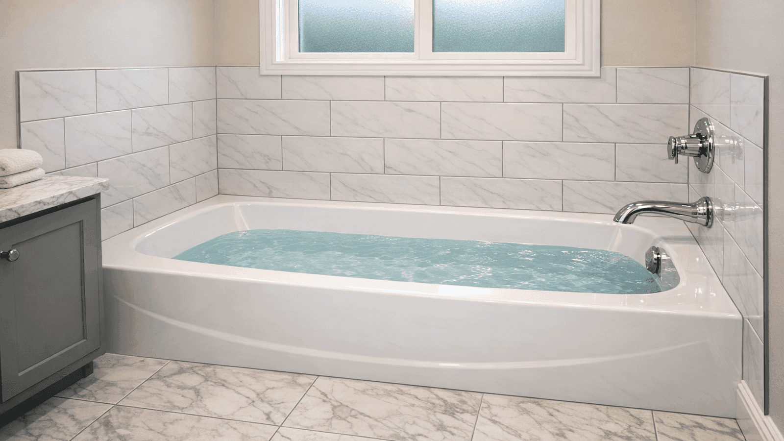 Finished bathroom with newly installed white alcove bathtub, tiled surround with chrome fixtures, clean caulk lines and polished chrome hardware