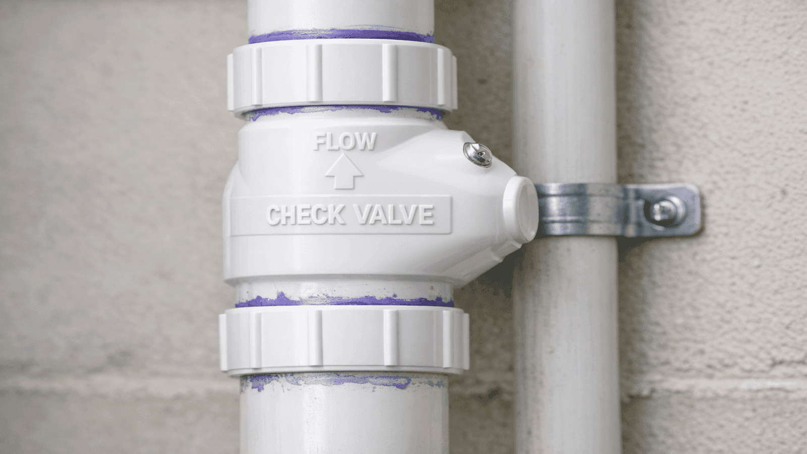 Close-up of check valve installed on vertical discharge pipe section above sump pump, flow direction marked