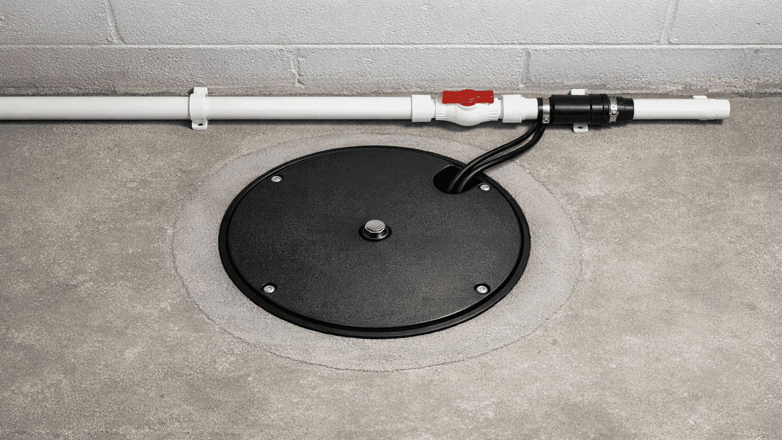 Finished sump pit with solid cover installed flush with basement floor, discharge pipe visible along wall