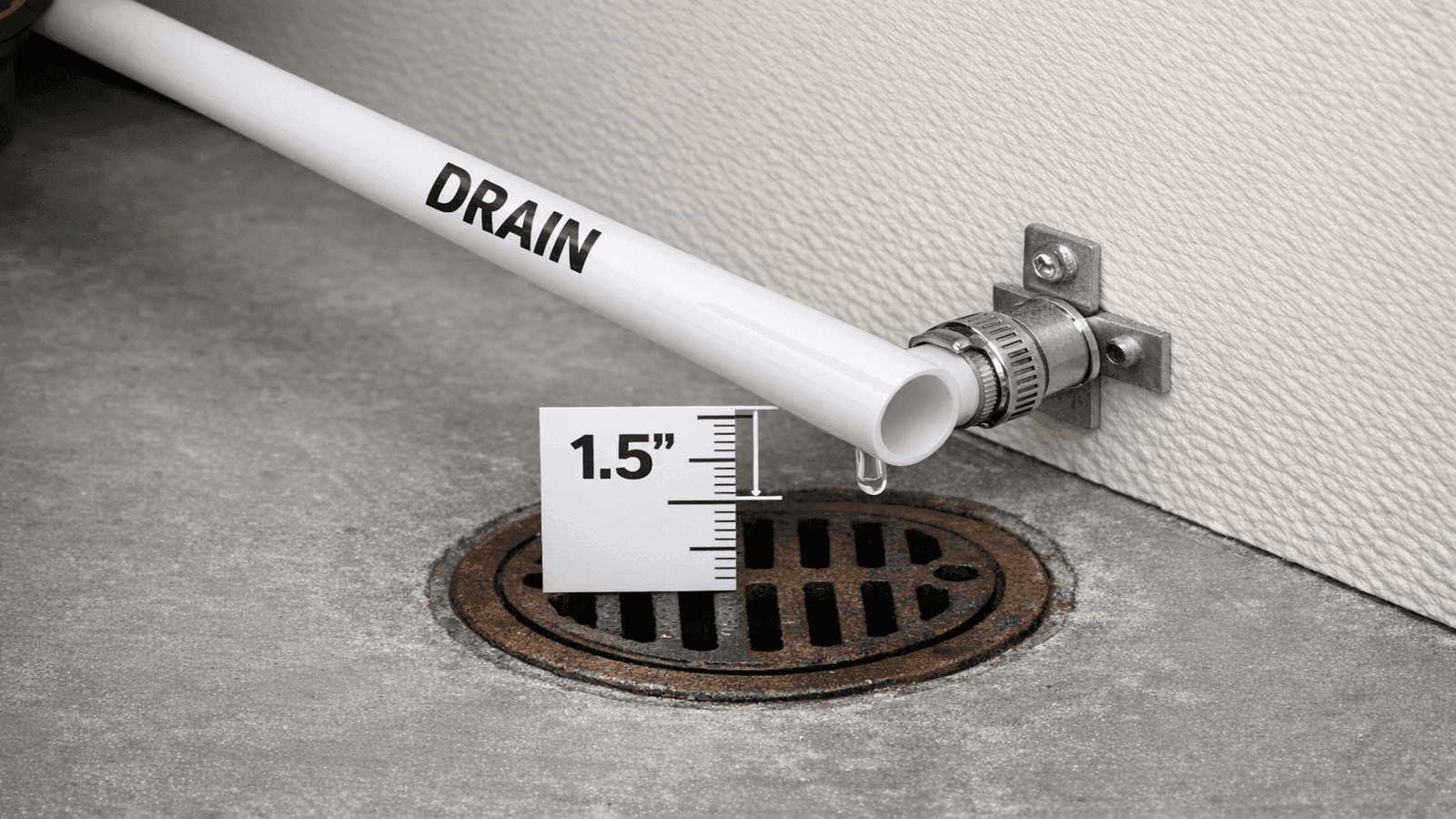 Drain line from water softener routed to a floor drain, PVC tube secured with hose clamp, 1.5-inch air gap visible above drain rim in utility room setting