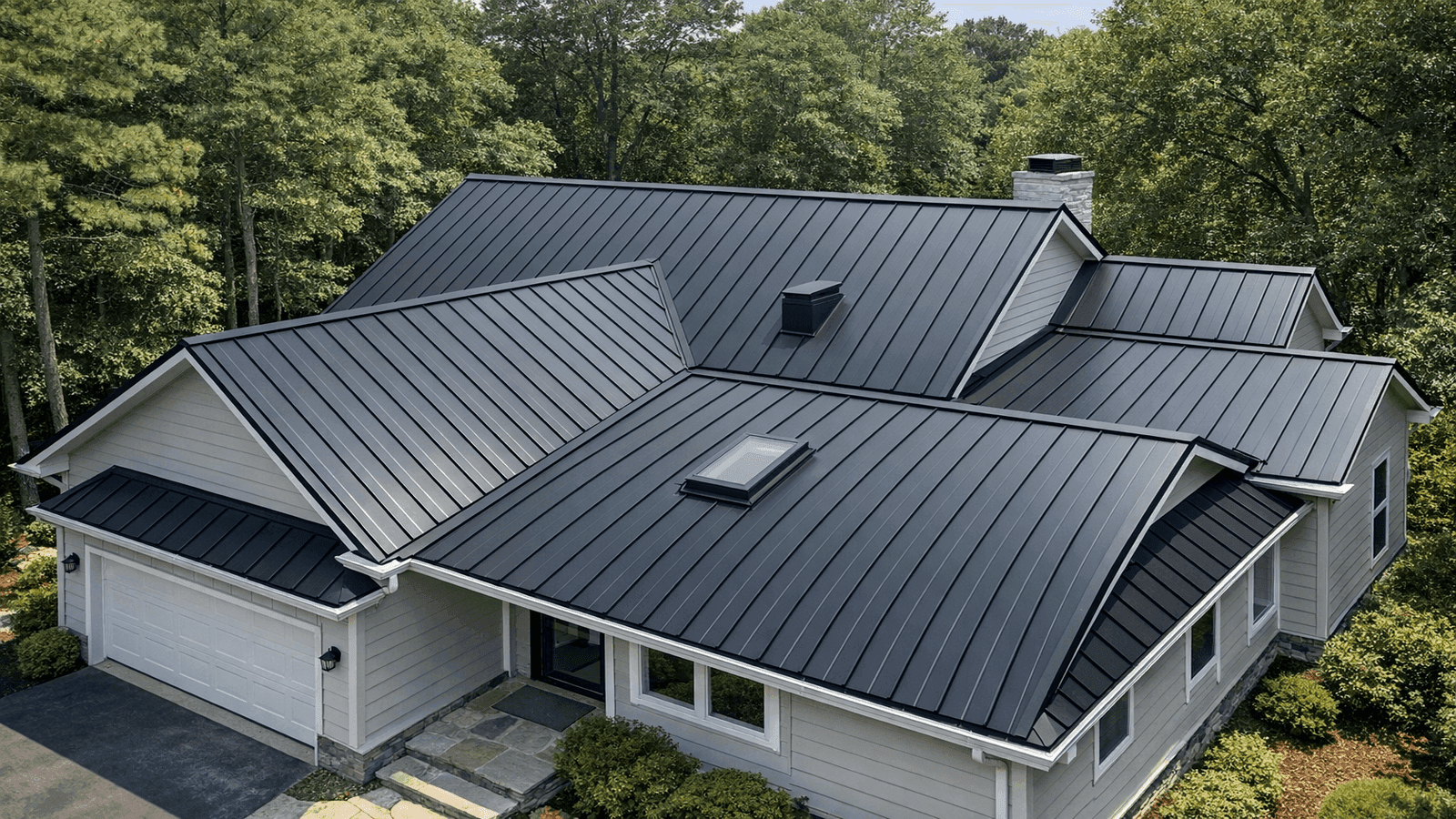 Aerial view of a residential home with standing seam metal roof in dark charcoal showing clean panel lines and concealed fasteners surrounded by mature trees