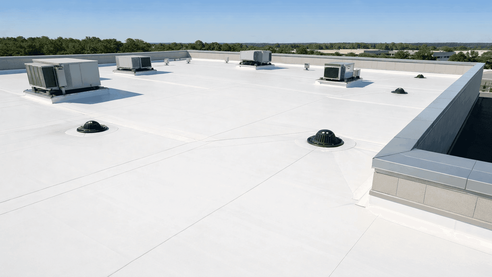 Aerial view of a well-maintained commercial building with a white TPO flat roof membrane, clean drains, and properly flashed HVAC curbs