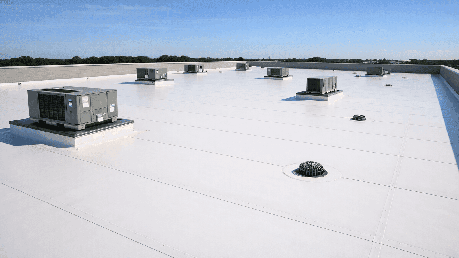 Wide view of a white TPO commercial flat roof showing parallel heat-welded seam lines, HVAC equipment on flashed curbs, and drain covers
