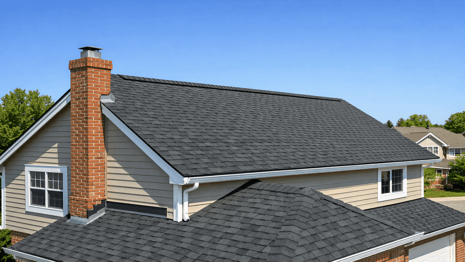 Completed residential roof installation showing clean architectural shingle lines, ridge vent, and chimney flashing on a suburban home