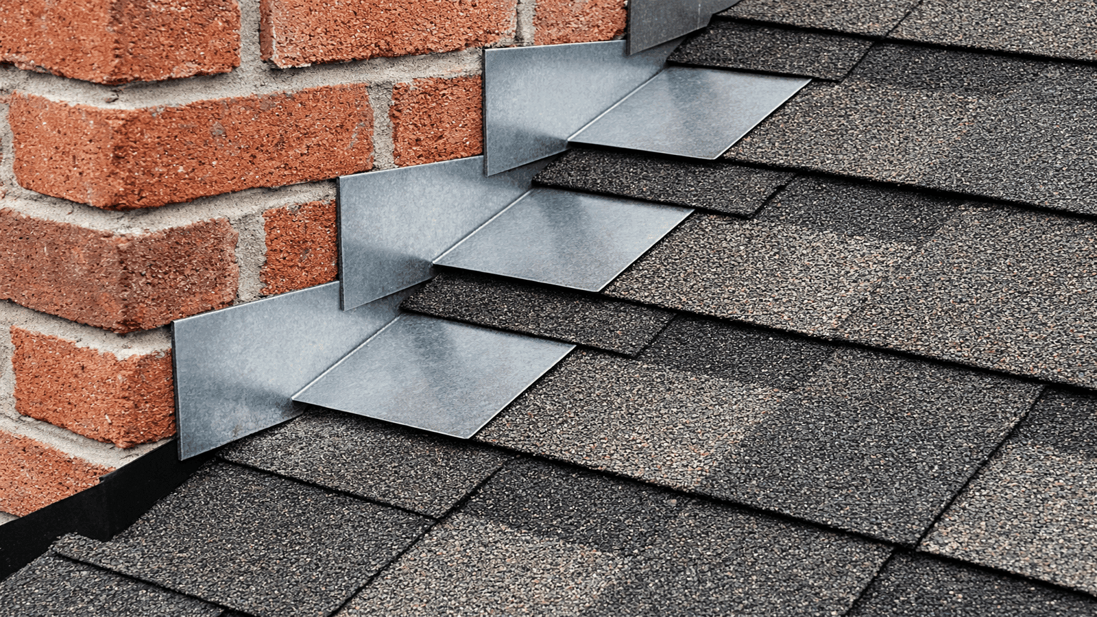 Properly installed step flashing showing L-shaped galvanized pieces alternating with shingle courses at a brick sidewall transition