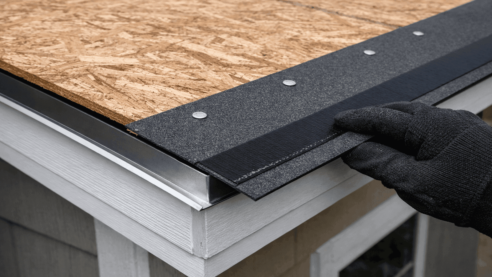 Close-up of eave edge showing OSB deck, metal drip edge, and purpose-made starter strip with sealant edge being positioned at correct quarter-inch overhang before asphalt shingle installation