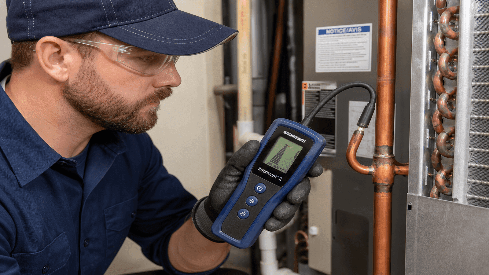 HVAC technician using an electronic leak detector along copper refrigerant lines near an indoor evaporator coil